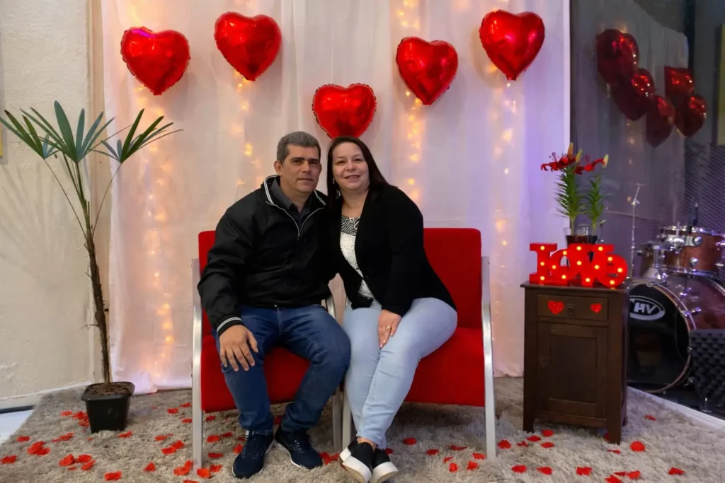 Casal posando em um espaço decorado com corações, luzes e pétalas durante o jantar de casais realizado na Igreja Adore