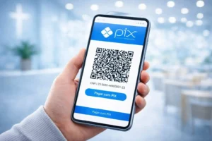 Mão segurando celular com QR Code Pix na tela para contribuição de dízimos e ofertas da Igreja Adore